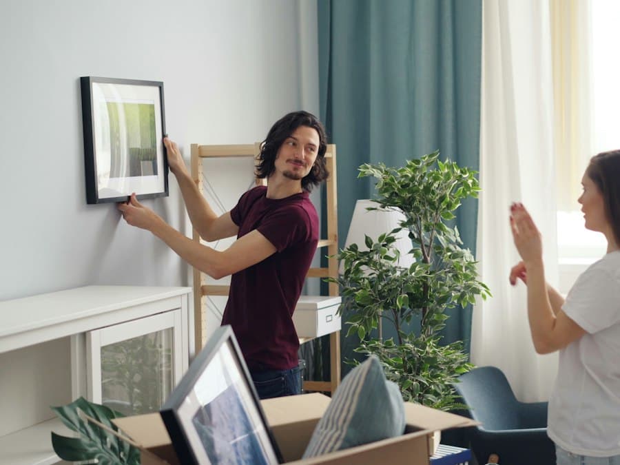 A man hanging a framed picture in a bright living room while unpacking boxes